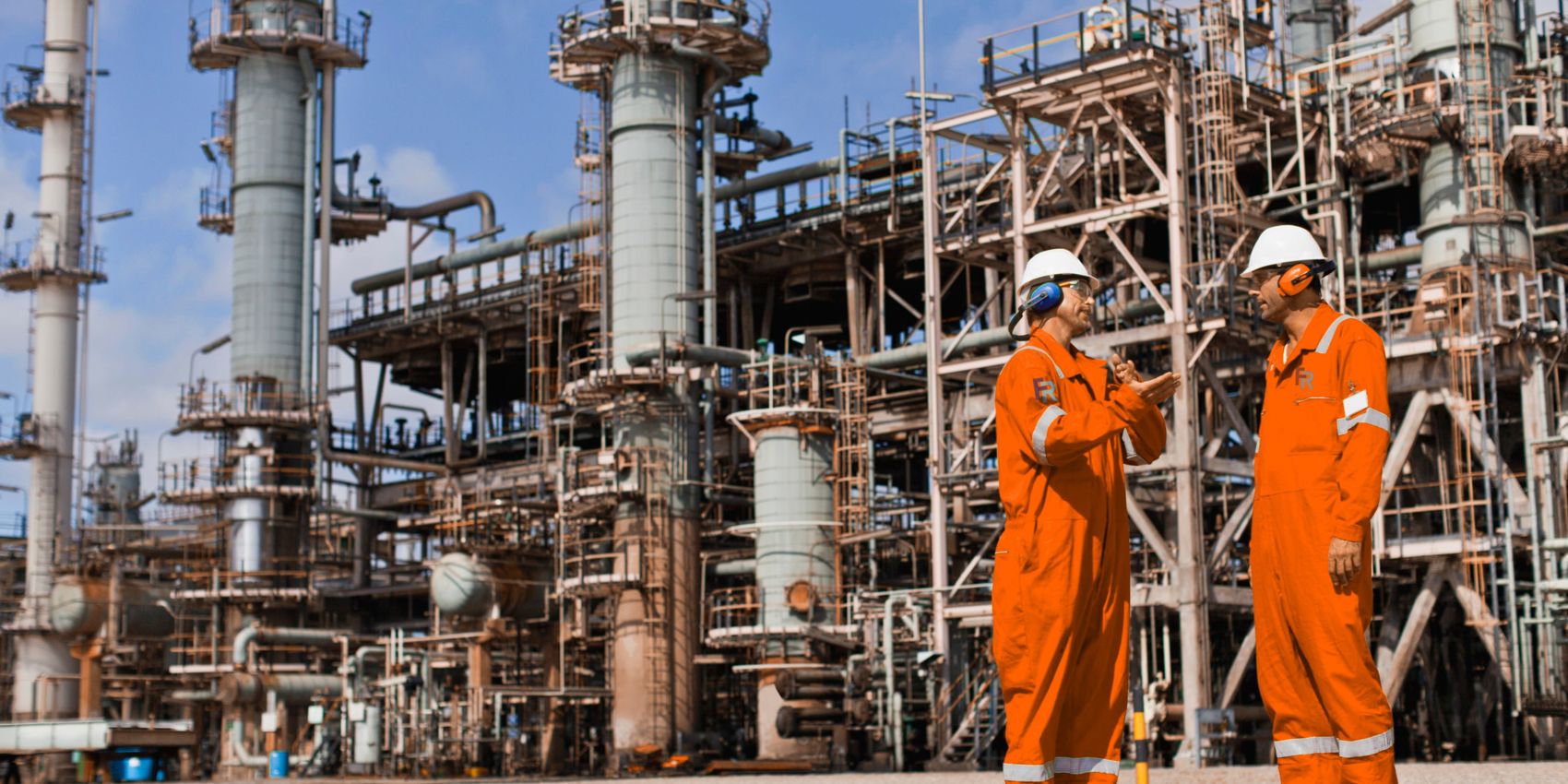 Two FosRich crew members in orange overalls at a refinery